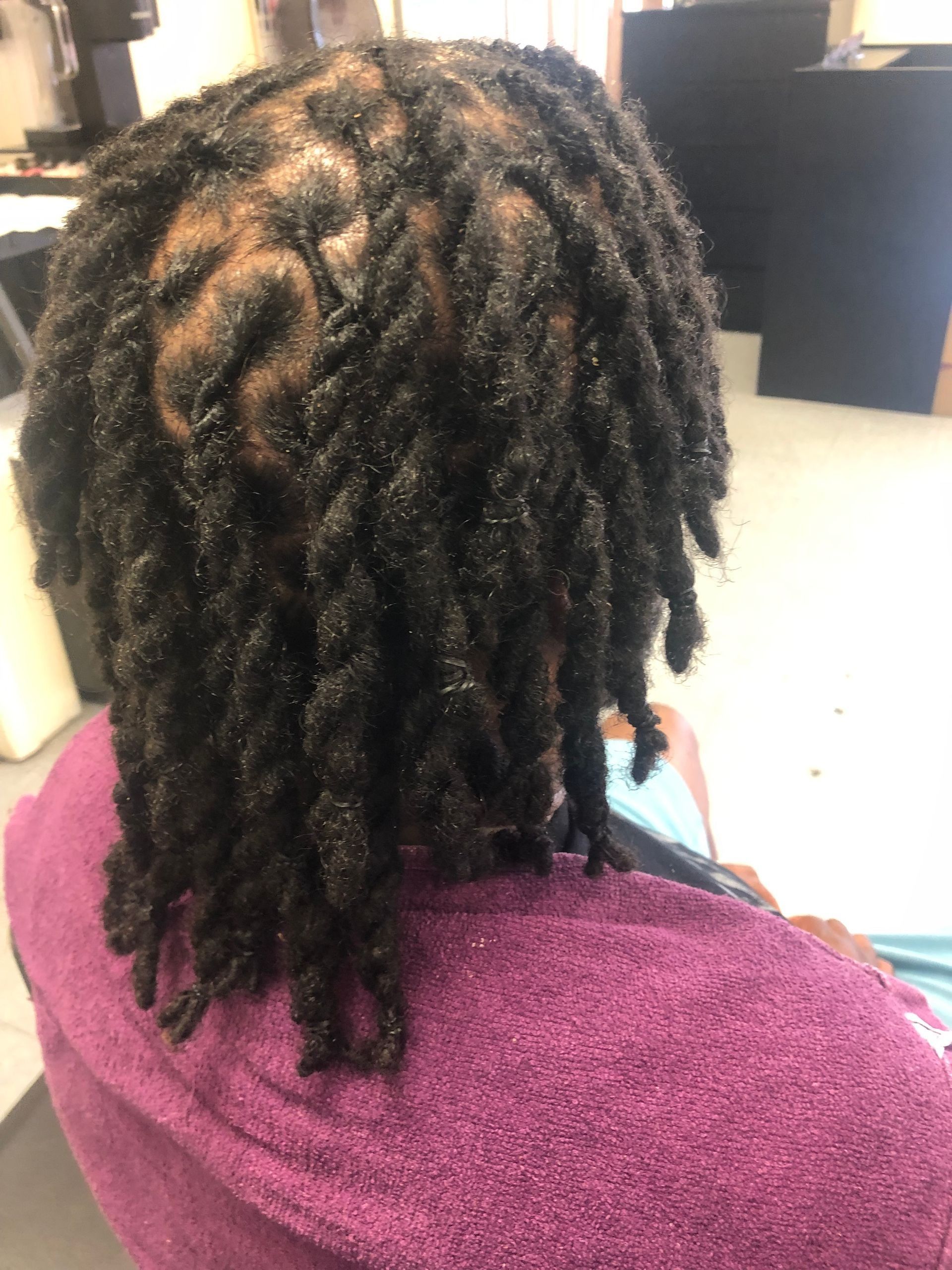 Person with dark, shoulder-length dreadlocks, sitting with a purple towel around their shoulders.