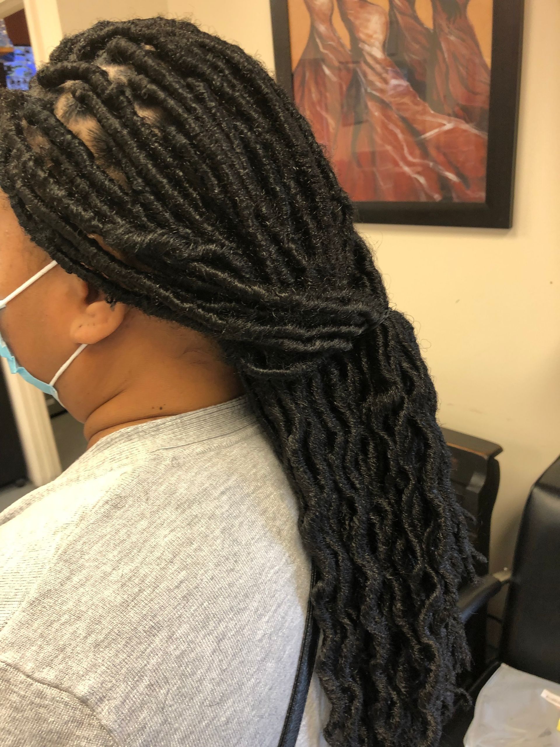 Person with dark locs pulled into a ponytail, wearing a gray shirt and a white mask.