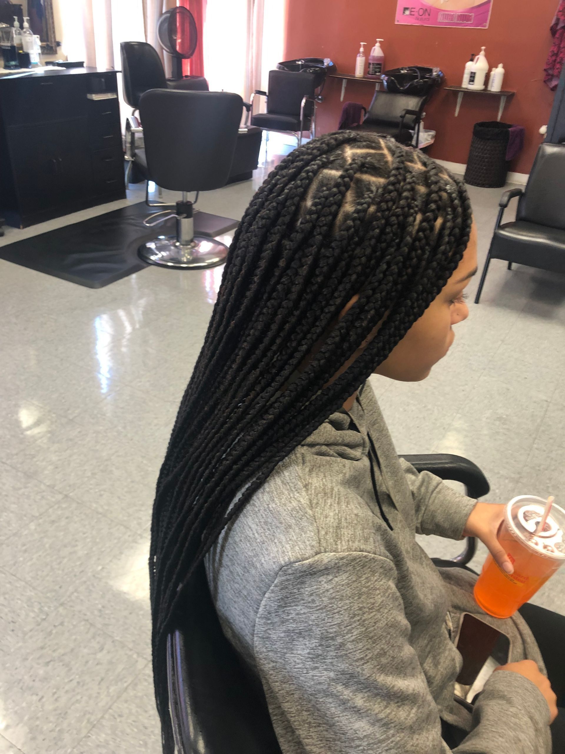 Woman with box braids in a salon holding a drink, seated in a chair.