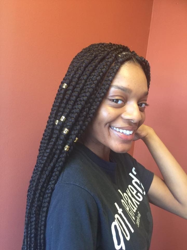 Woman with box braids smiling, posing in front of a peach-colored wall, wearing a black t-shirt.
