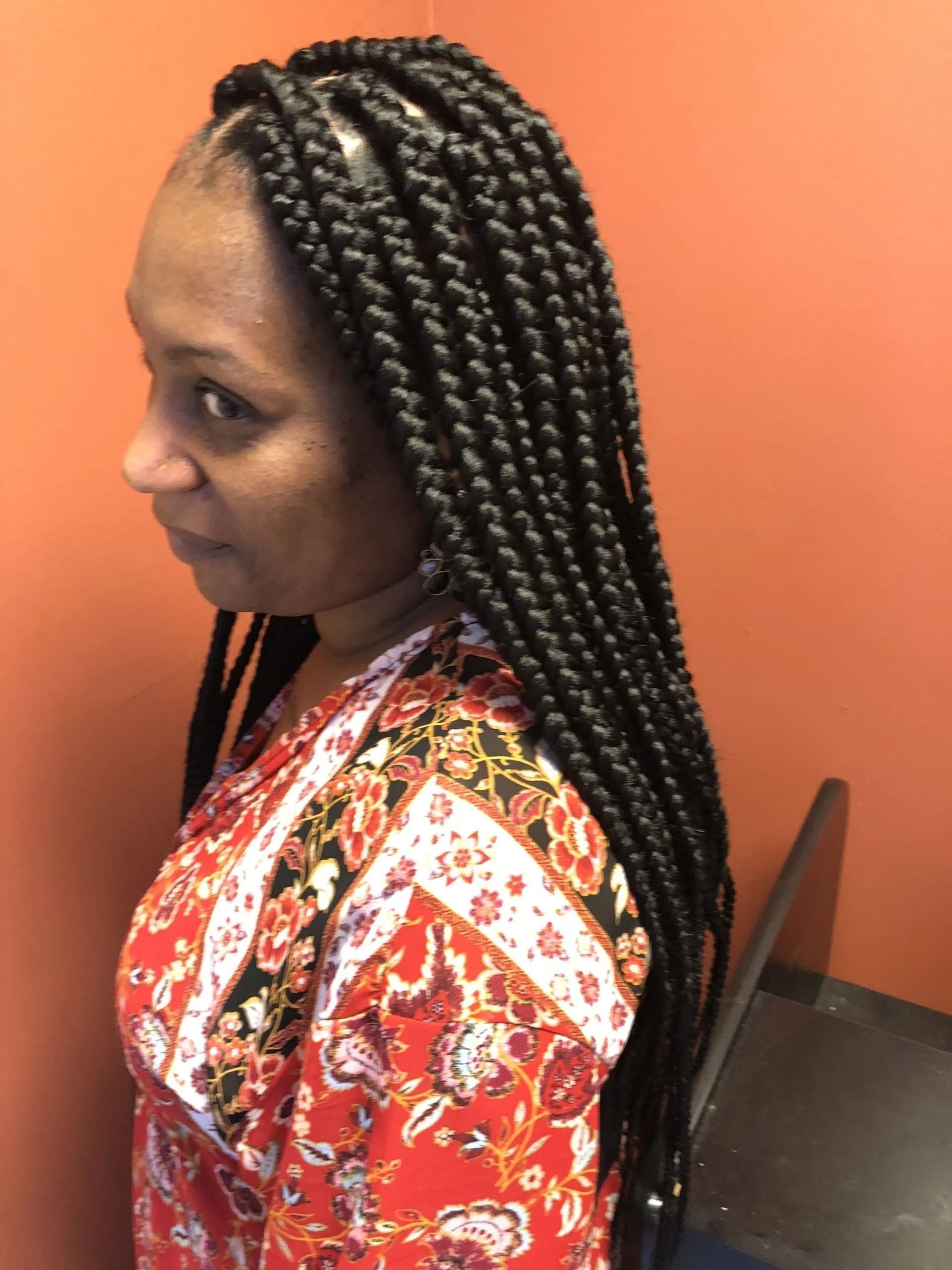 Woman with box braids in front of an orange wall, wearing a red patterned shirt.