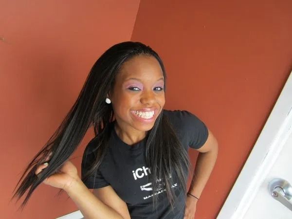 Woman smiling, wearing black t-shirt, long black hair, in front of orange wall.