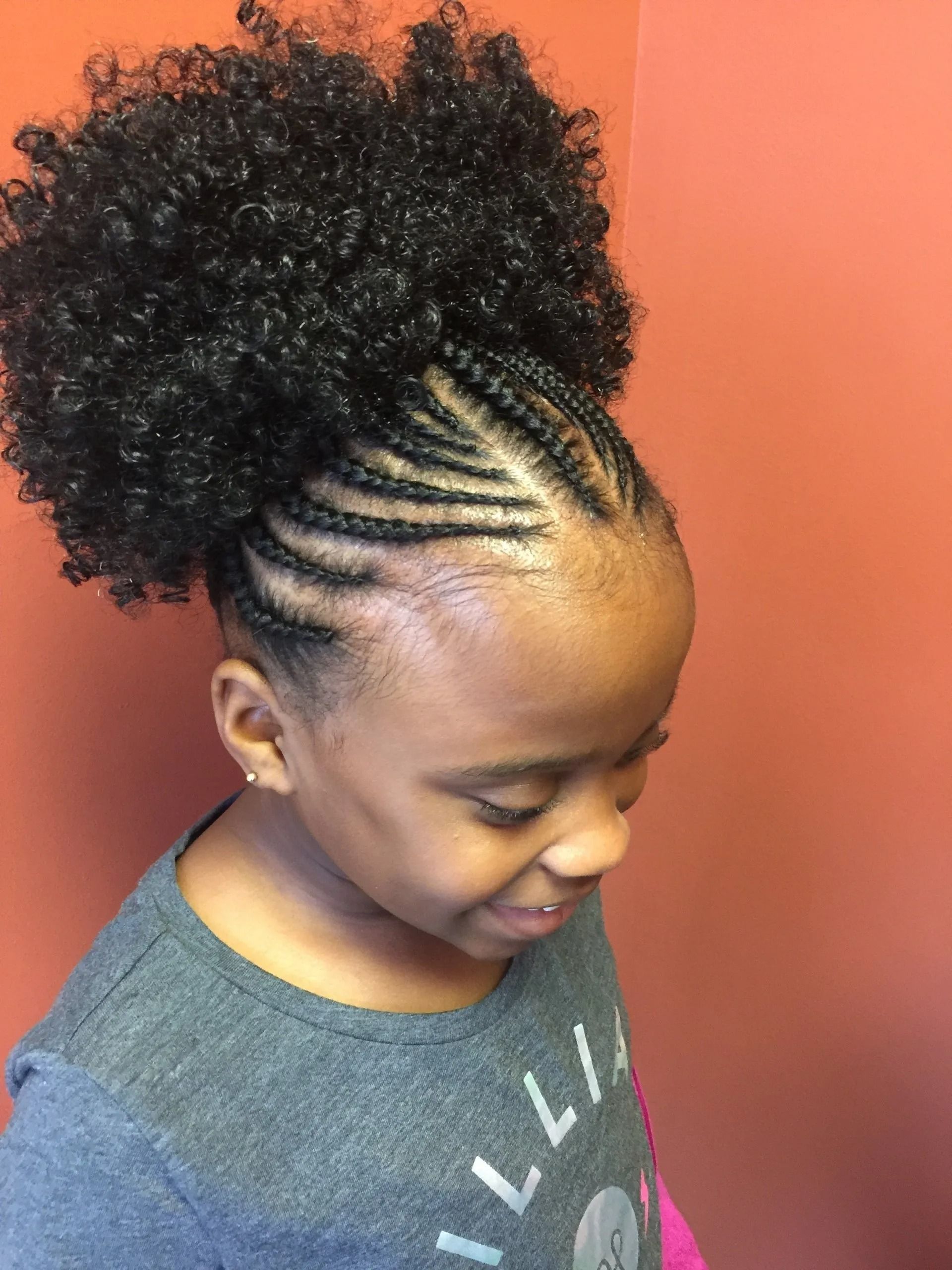 Girl with cornrows and a curly bun smiling, wearing a gray shirt.