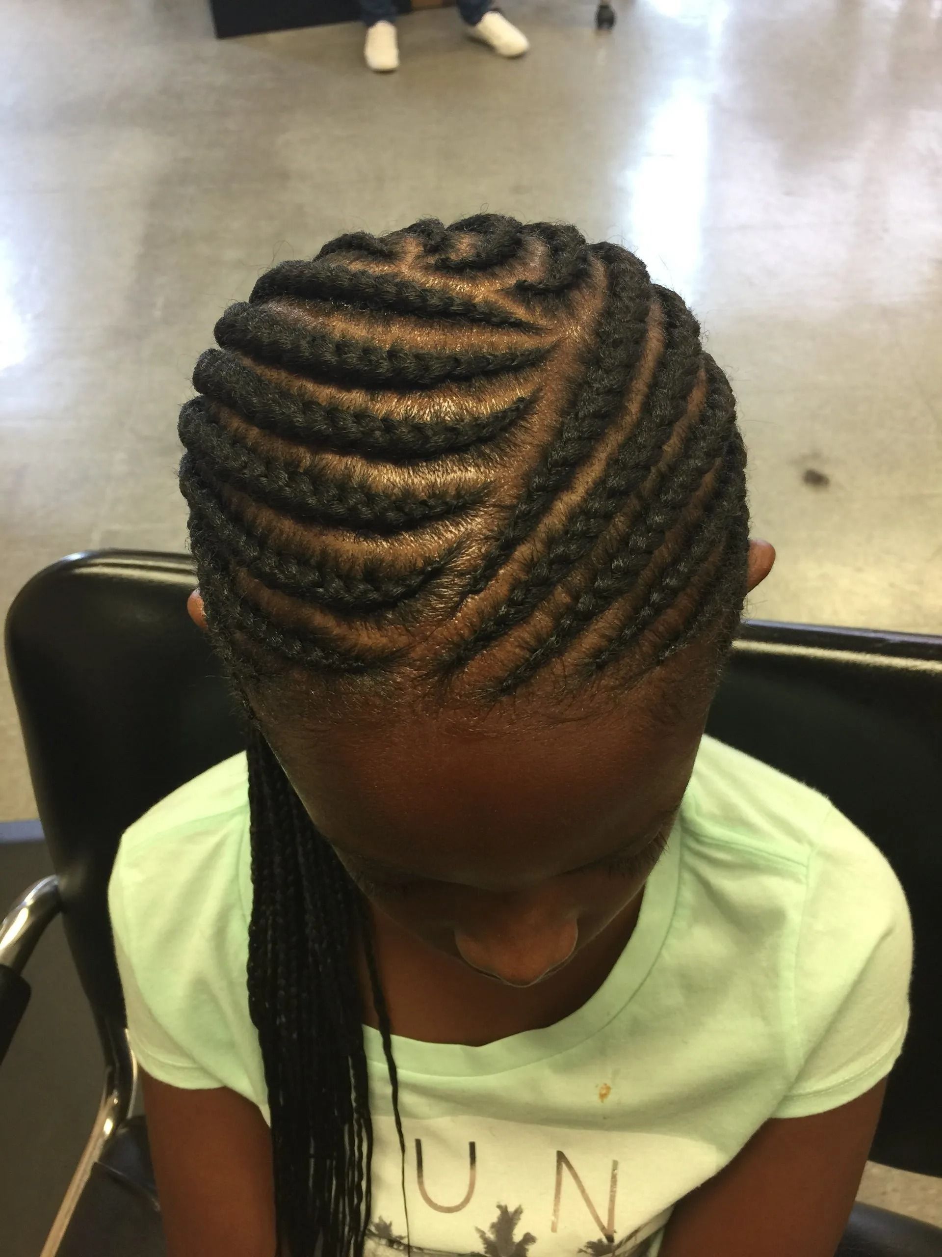 A Black girl with braided hair styled in a diagonal pattern, wearing a mint green shirt.