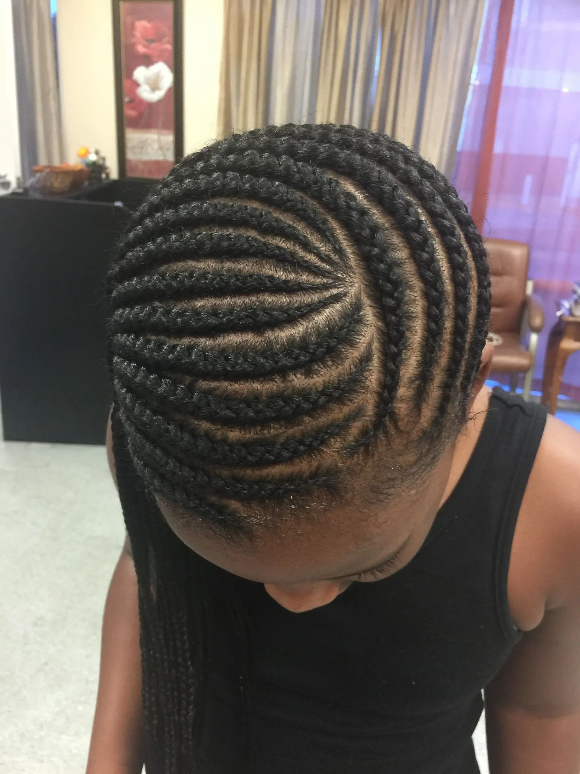 Close-up of a person with neatly braided black hair. Braids curve and spiral across the head.