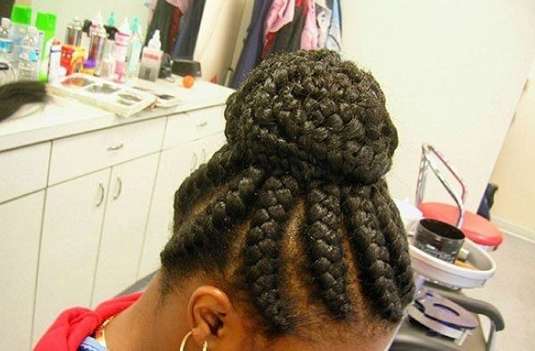 Black woman with braided cornrows styled into a high bun in a salon setting.