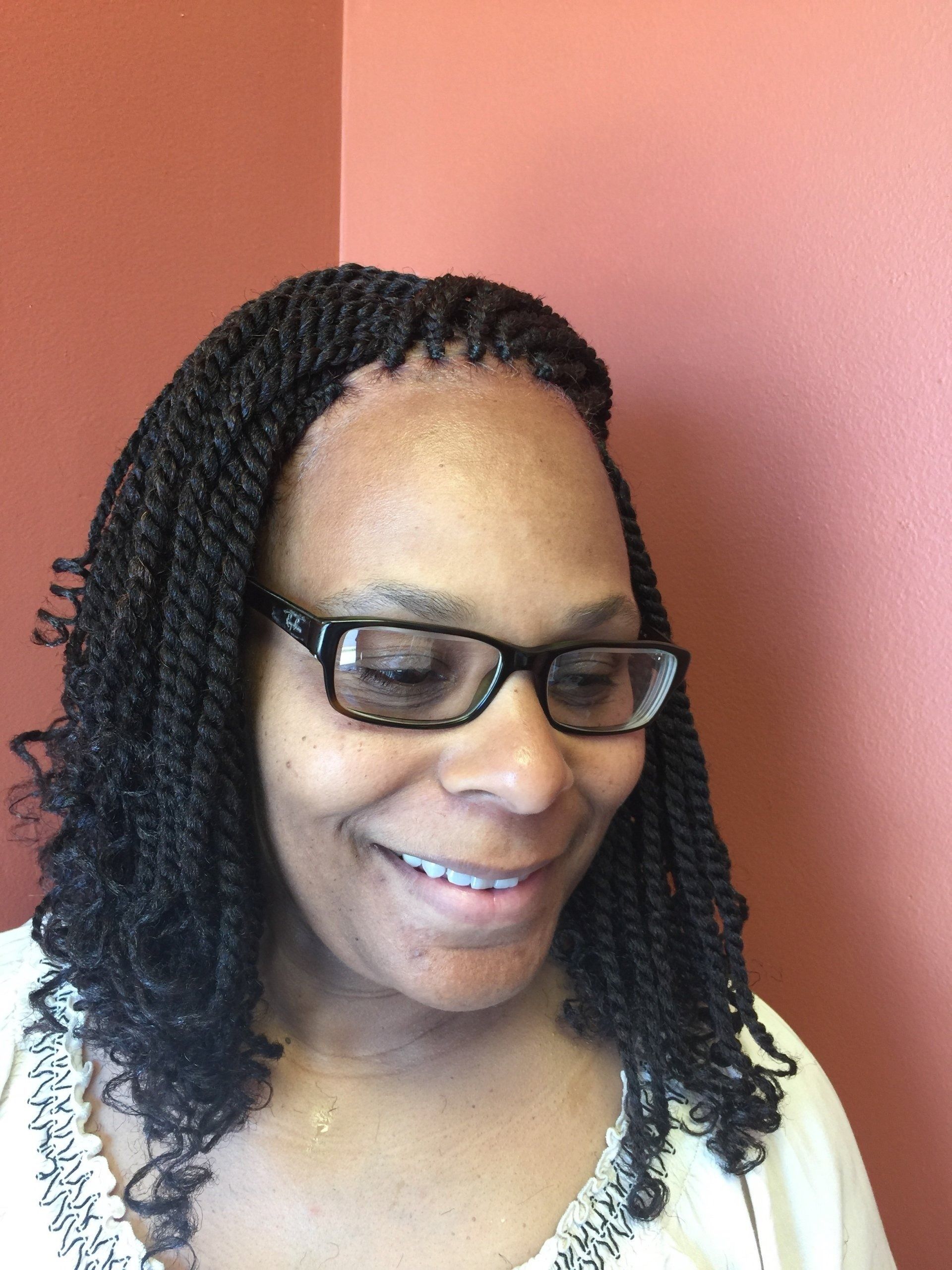 Woman with black twists, wearing glasses, smiling against an orange wall.
