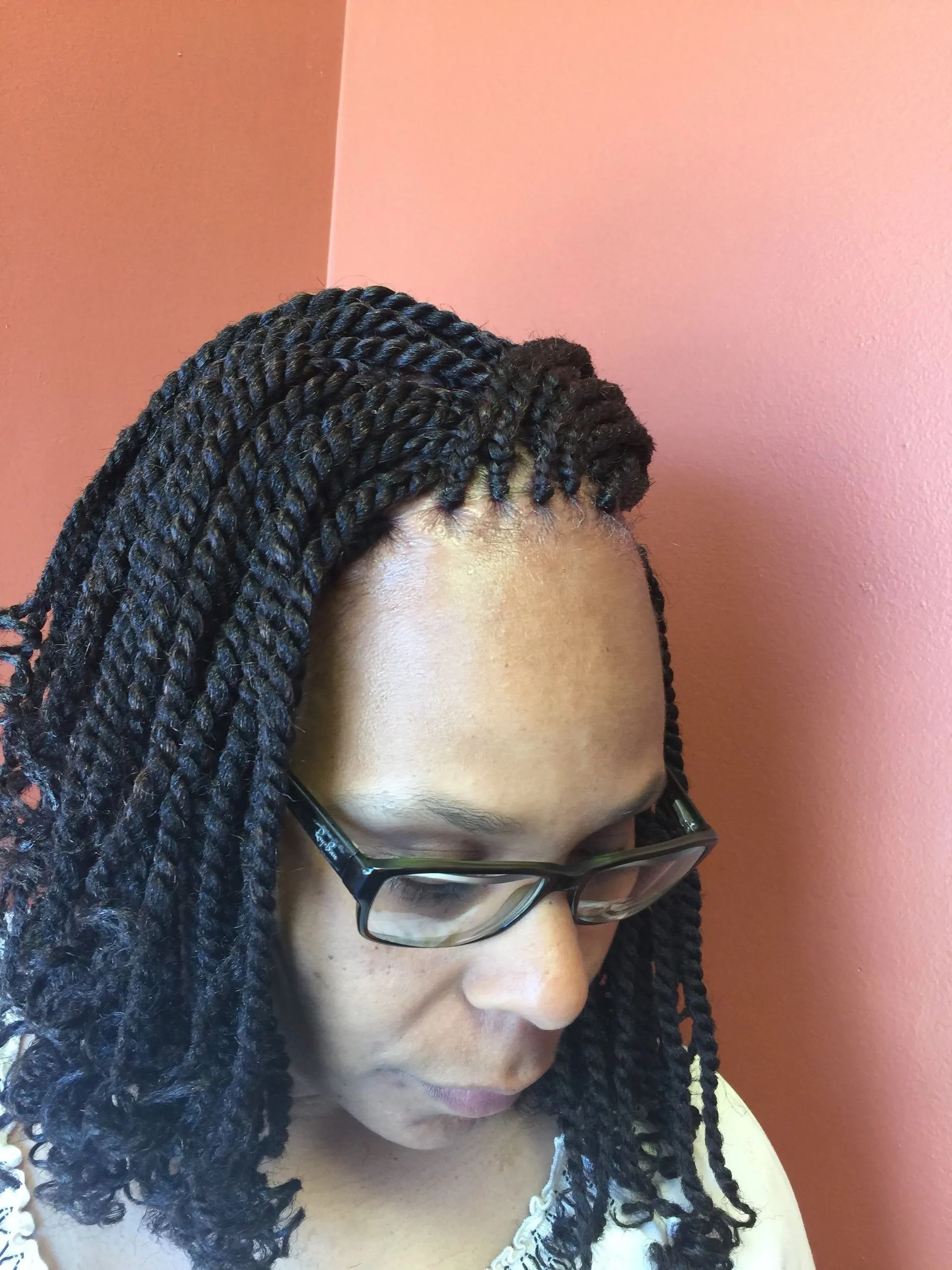 Woman with black twisted braids and glasses, looking down. Orange wall background.