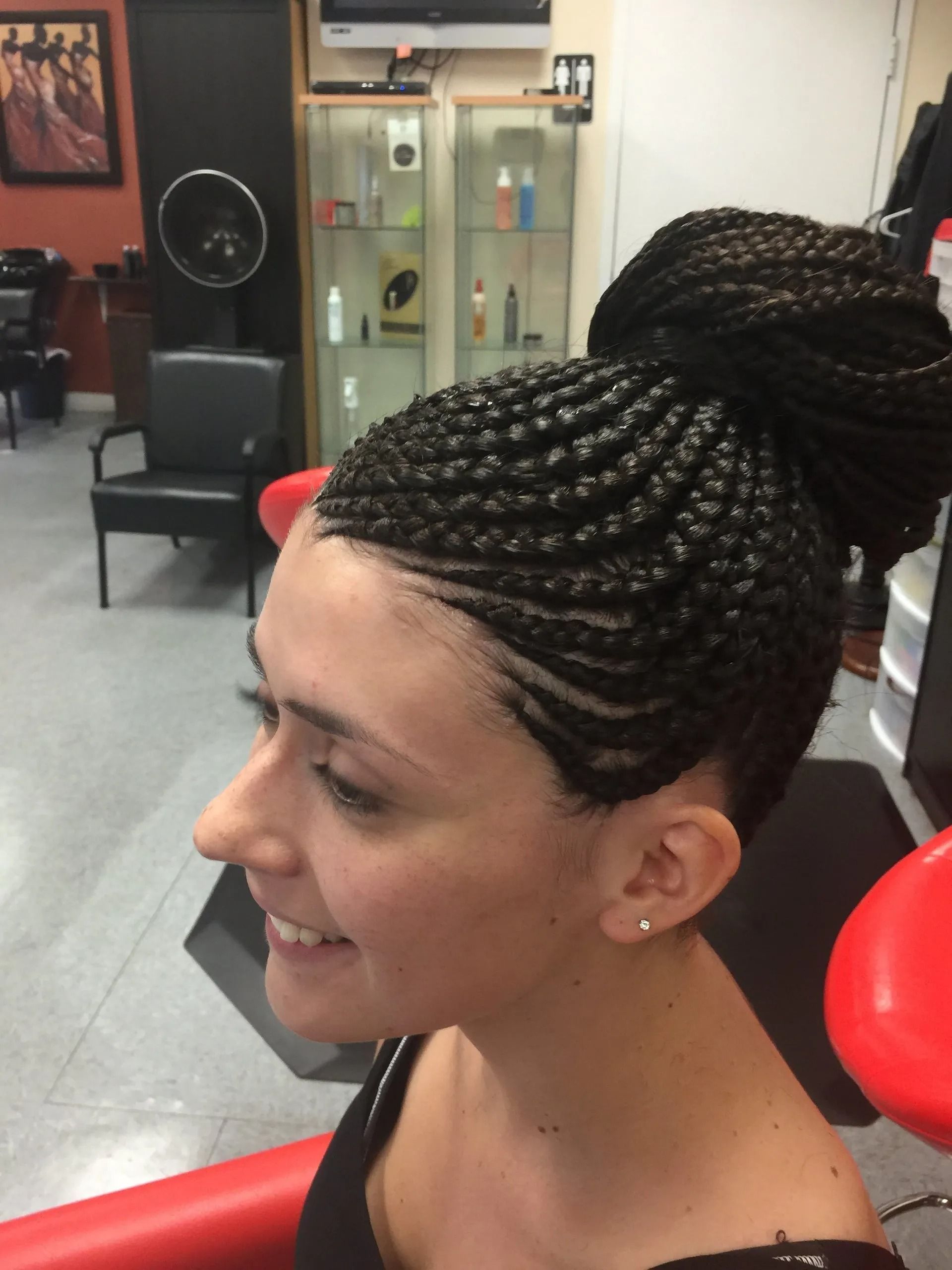Woman with cornrow braids up in a bun, smiling, in a hair salon.