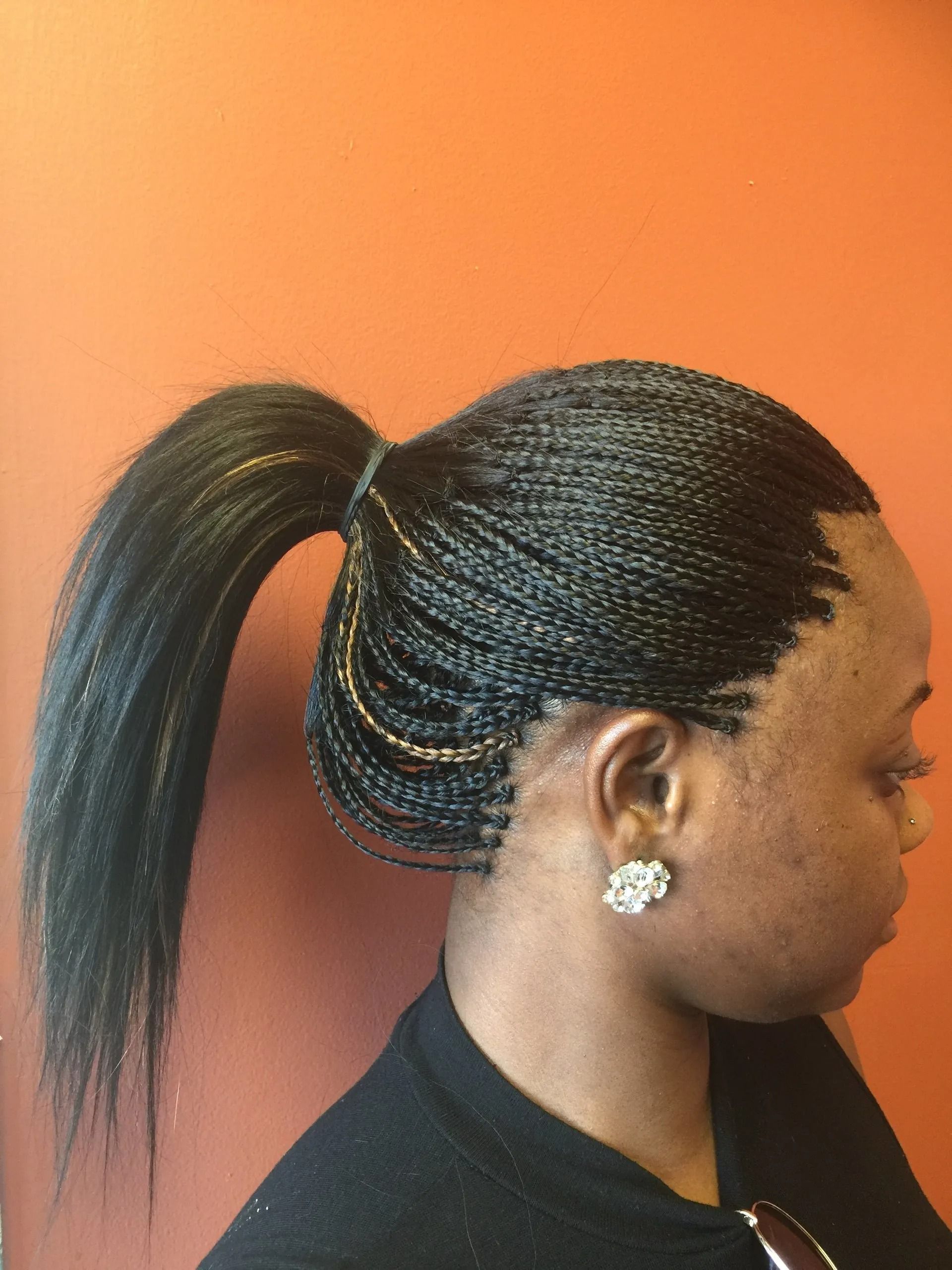 Woman with micro braids in a high ponytail against an orange wall.