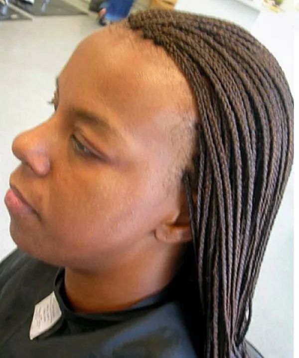 Woman with thin brown braids, looking left, wearing a black cape, in what appears to be a salon.