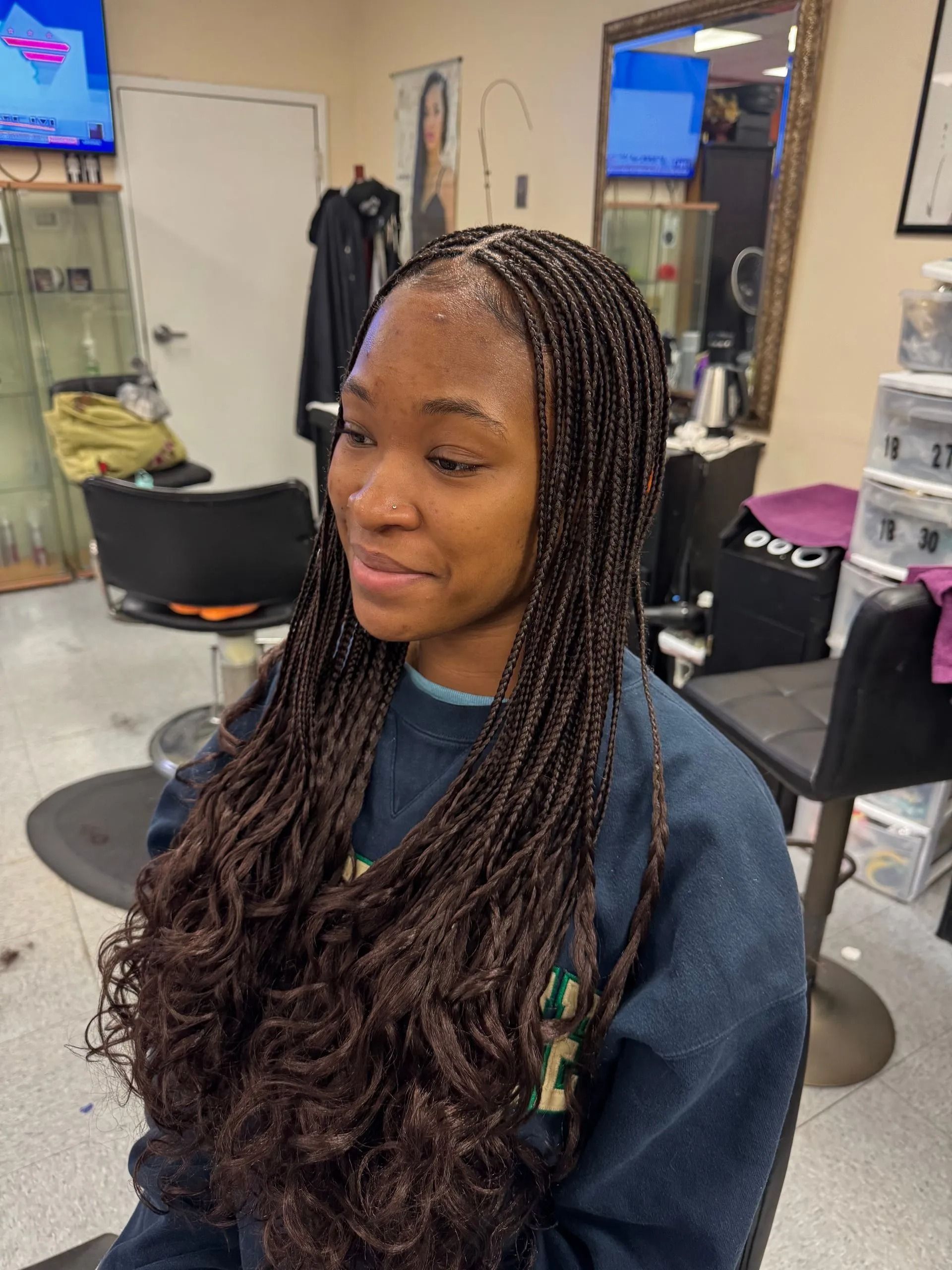 Woman with brown box braids and curly ends smiles in a hair salon.
