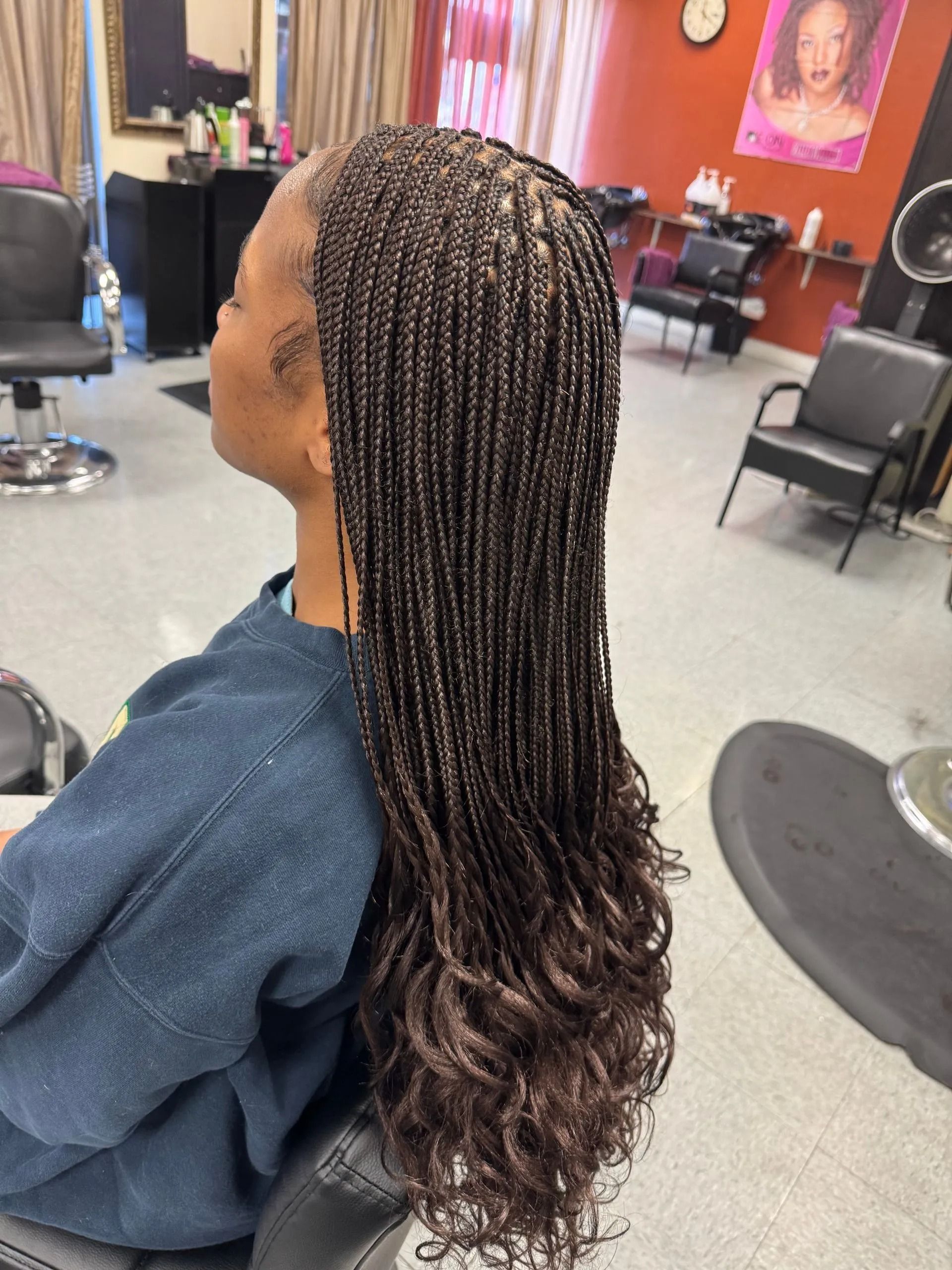 Woman with micro braids cascading into wavy ends, seated in a salon.