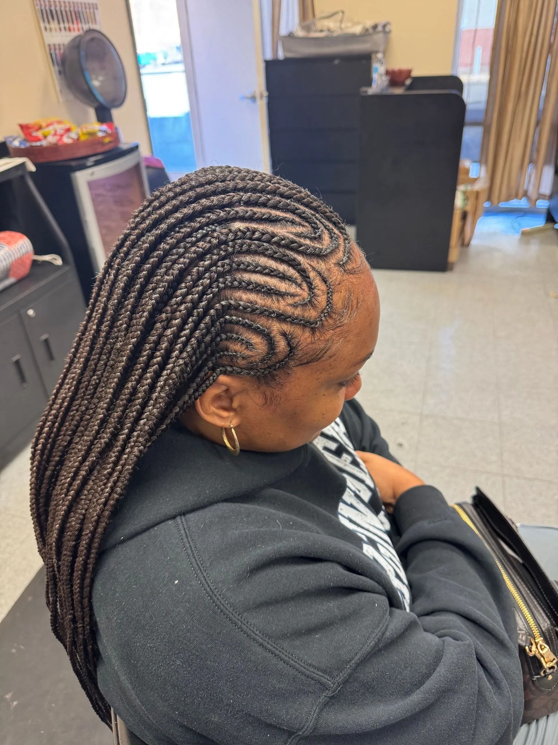 Woman with long box braids, some brown, in a salon. Braids are styled into a design on the side.