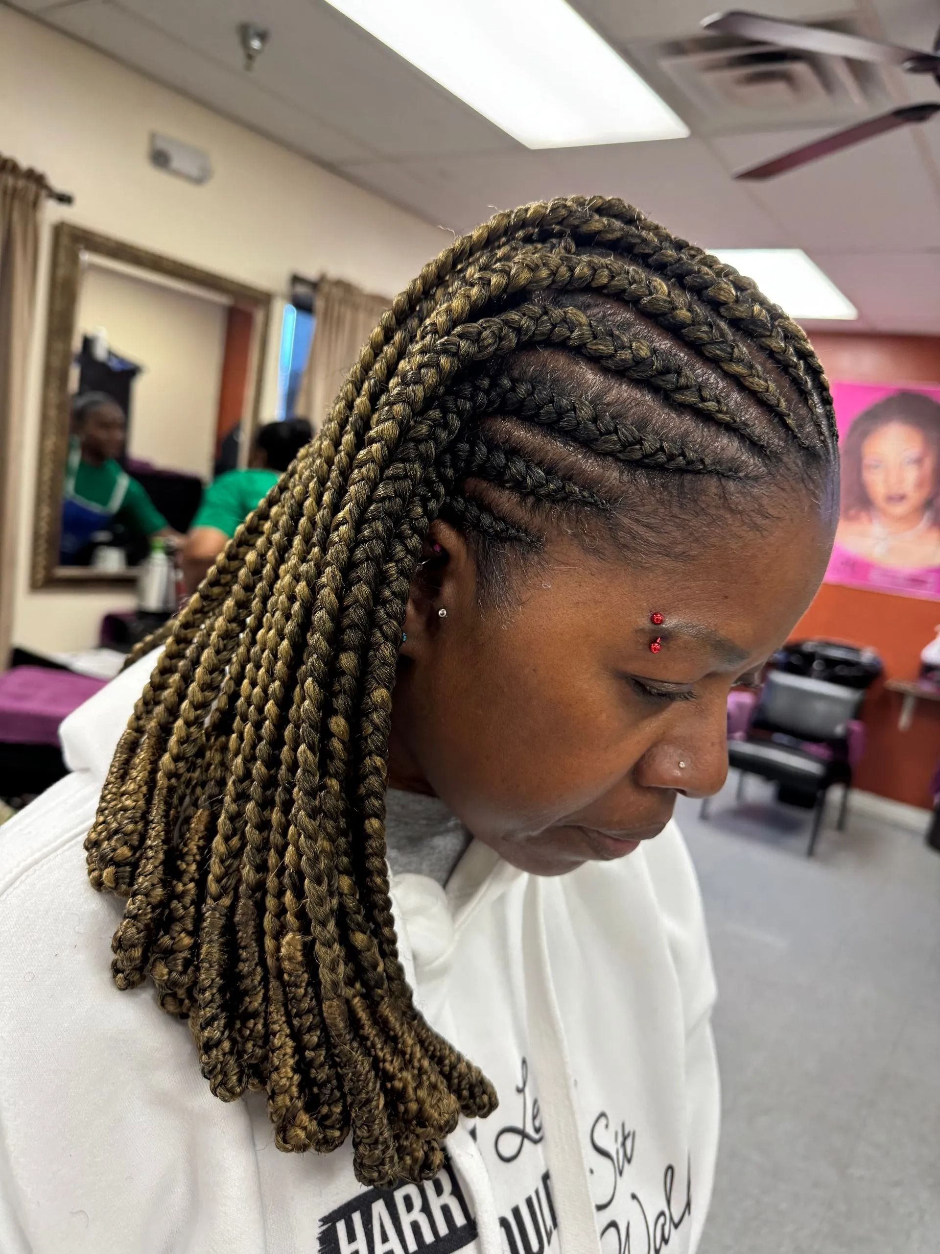 Woman with braided hair, light and dark brown, in a salon. She is wearing a white hoodie.