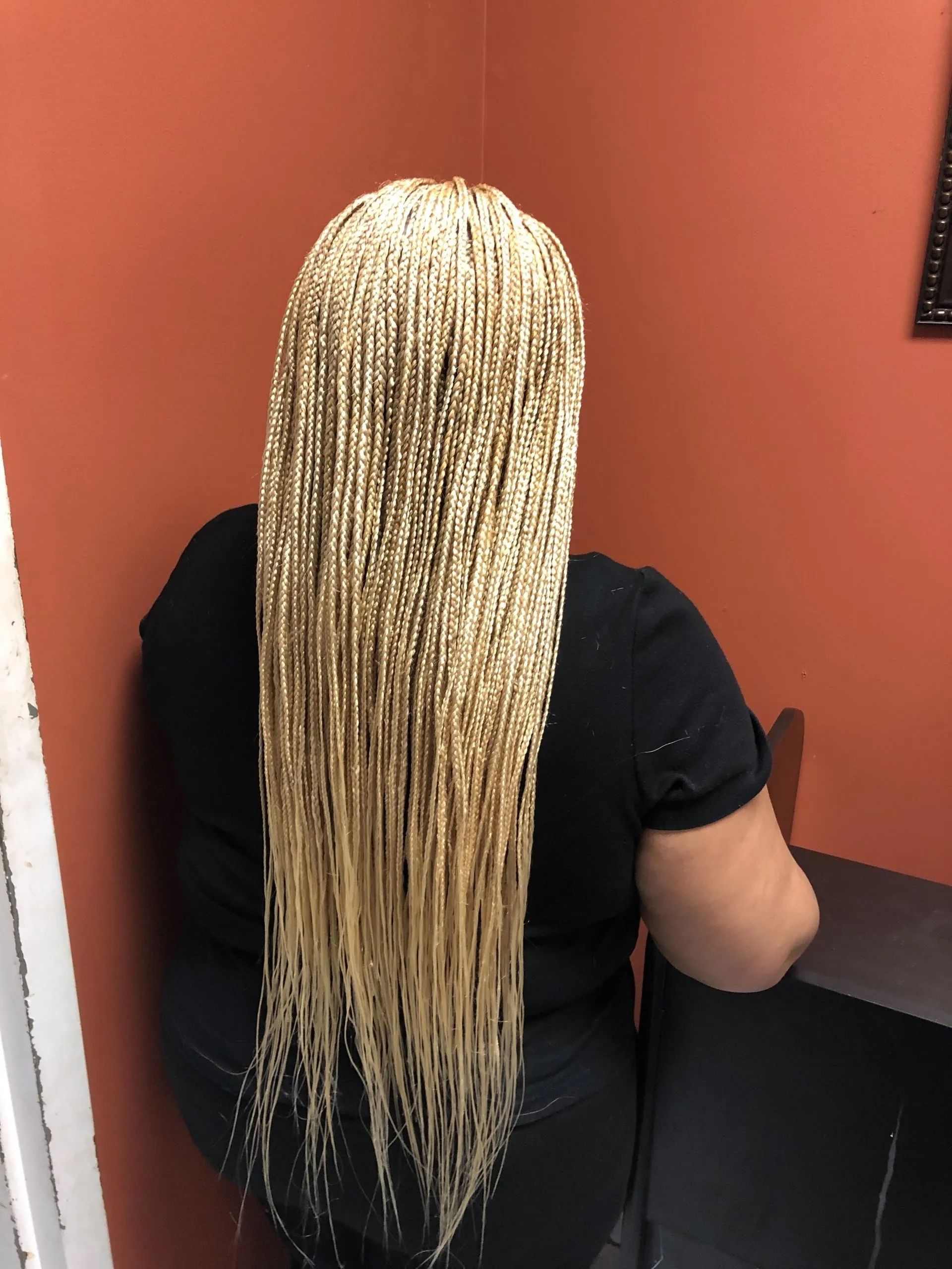 Woman with long blonde box braids stands against an orange wall.