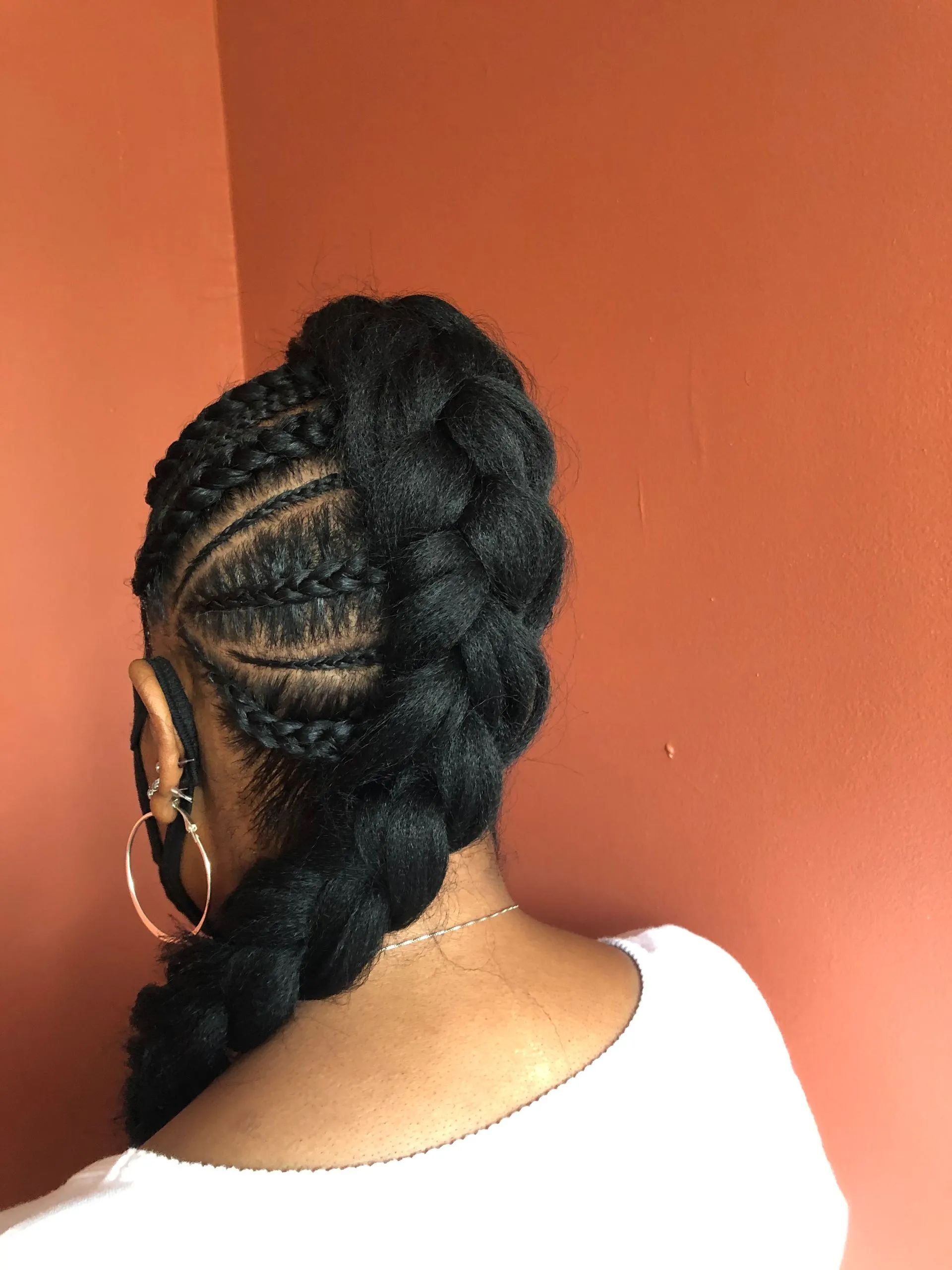 Woman with dark braided hairstyle and hoop earrings, against a peach wall.