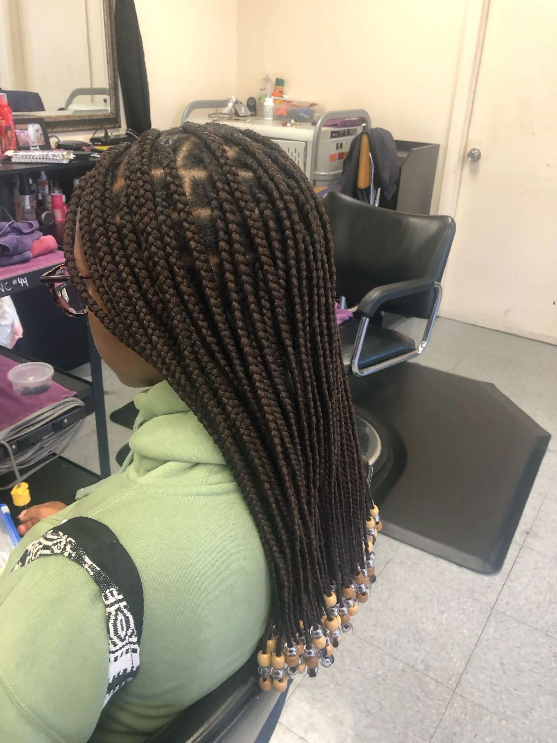 Woman with long, brown box braids in salon, hair styled with beads.