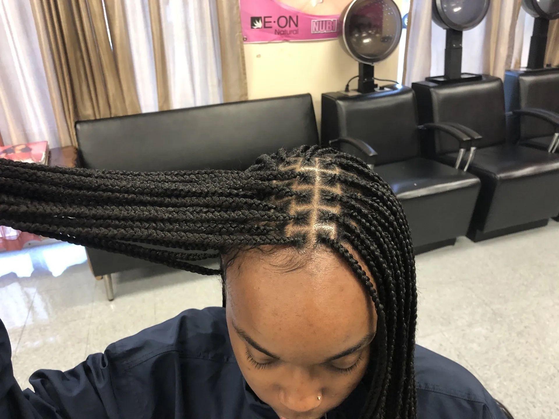 Woman with box braids in a salon. Braids are black, styled partially over her forehead.