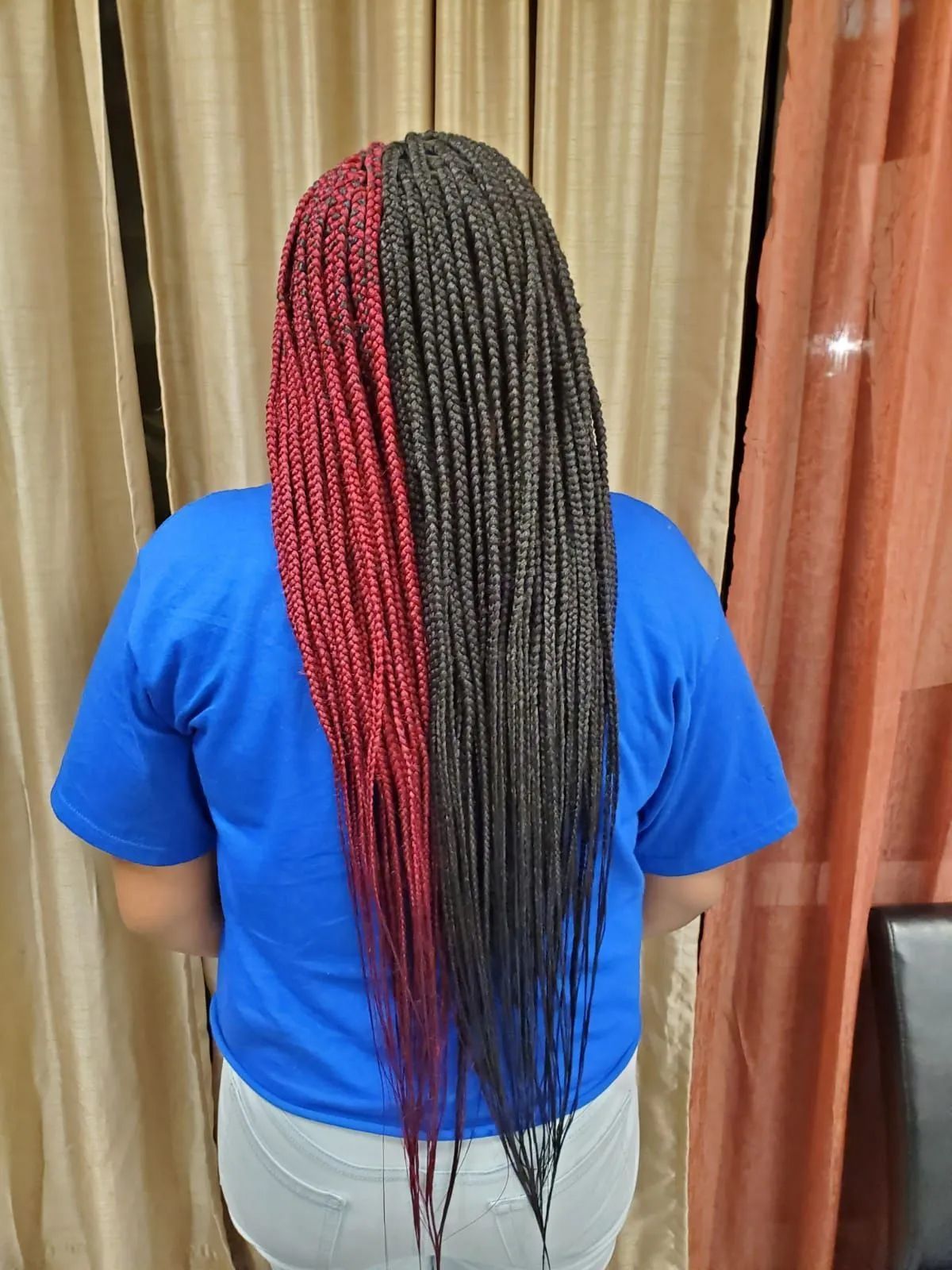 Person with long, half-red and half-black braided hair. Wearing a blue shirt and white shorts.