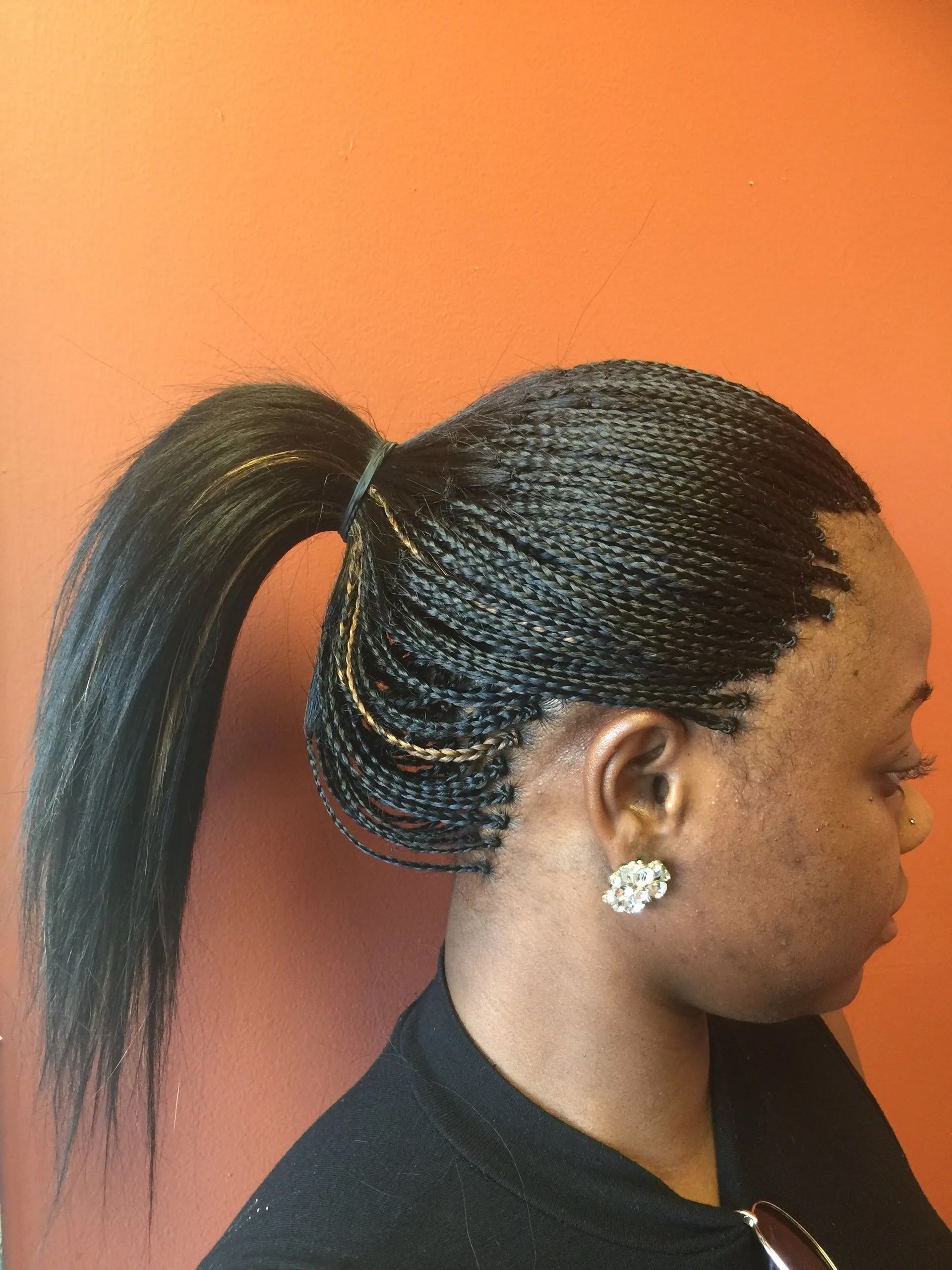 Black woman with micro braids in a high ponytail, against an orange wall.