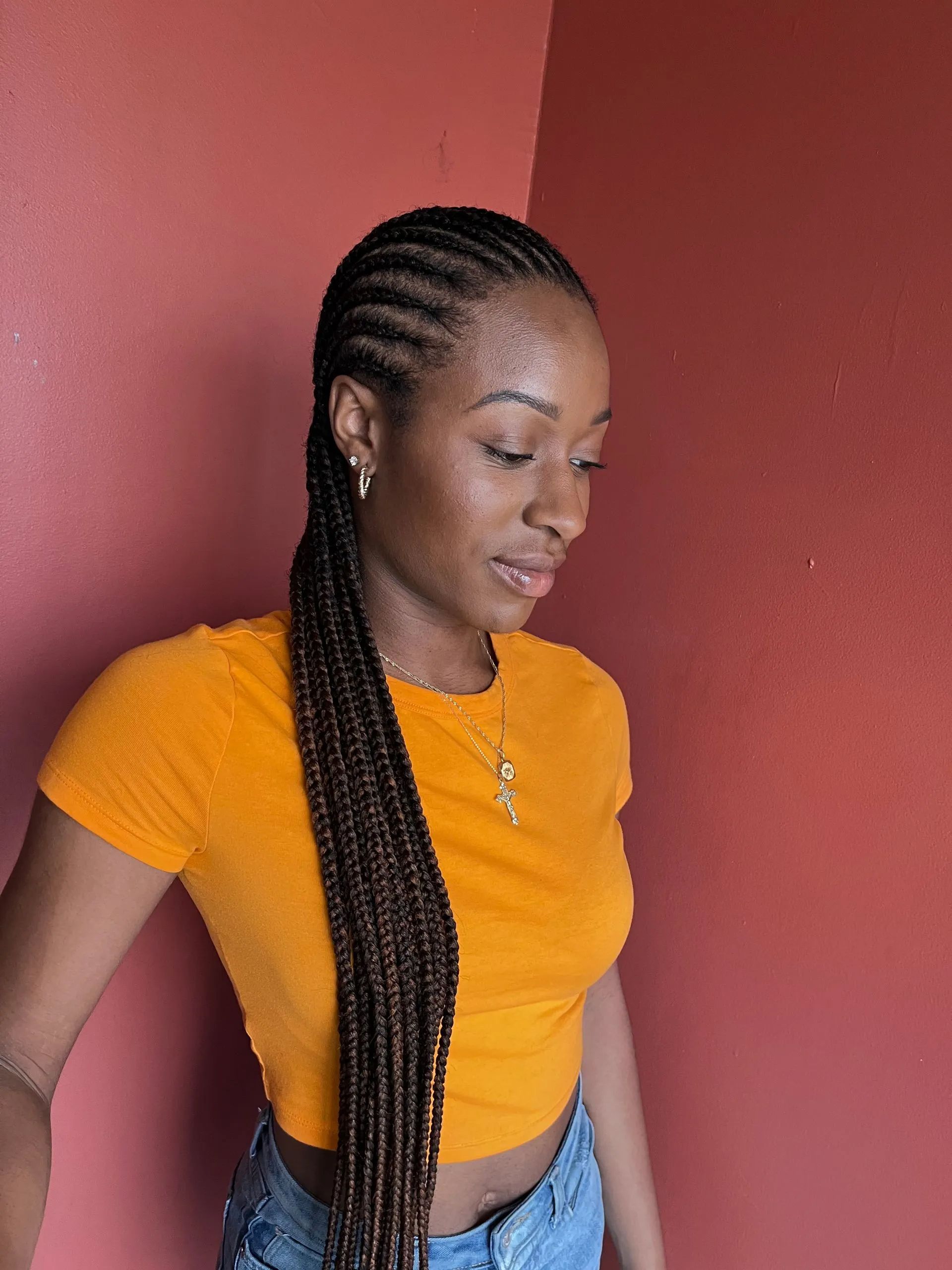 Woman with braided hair in an orange top, looking down against a red background.