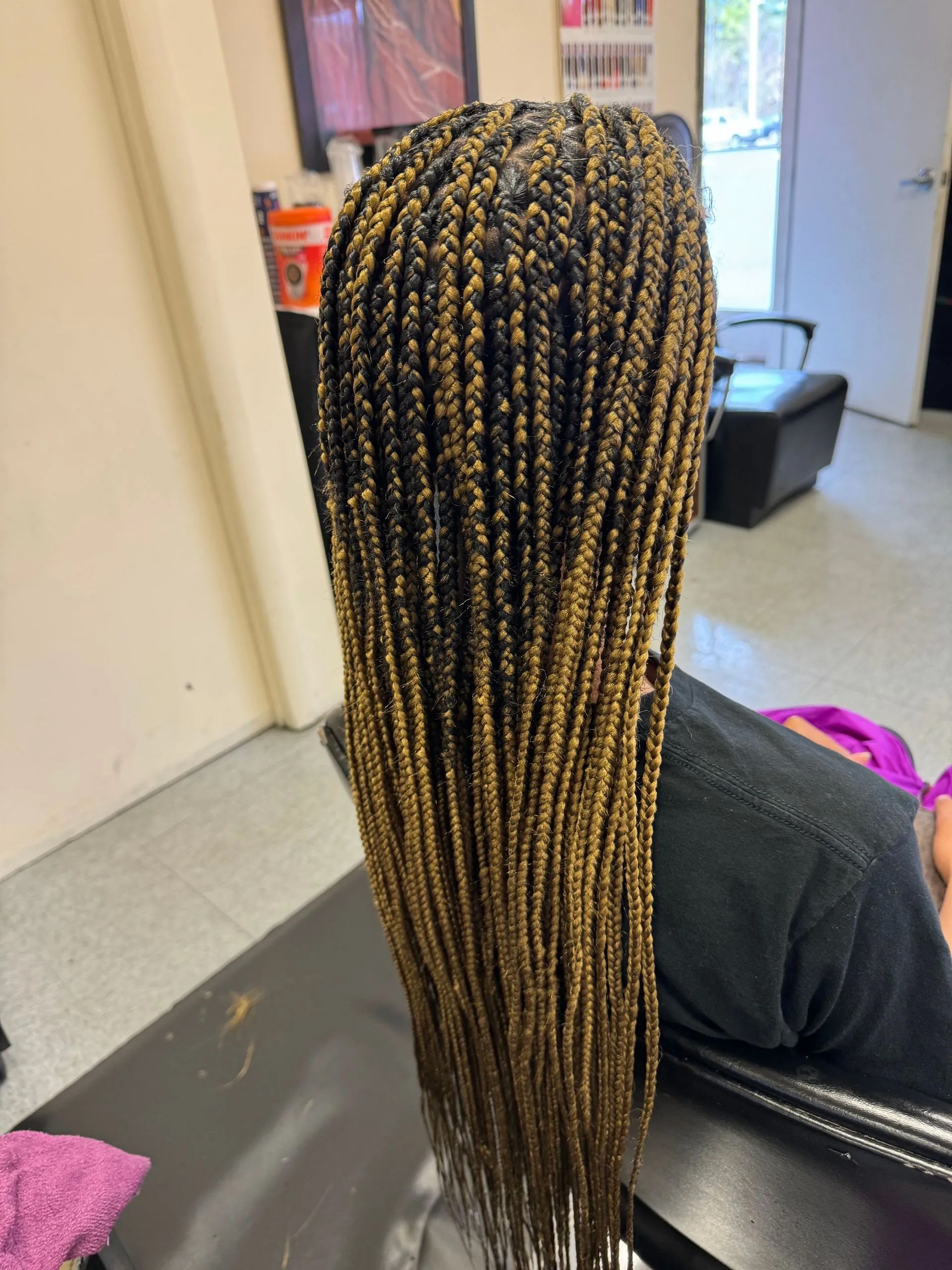Person with long box braids, black and gold ombre, sitting in a salon chair.