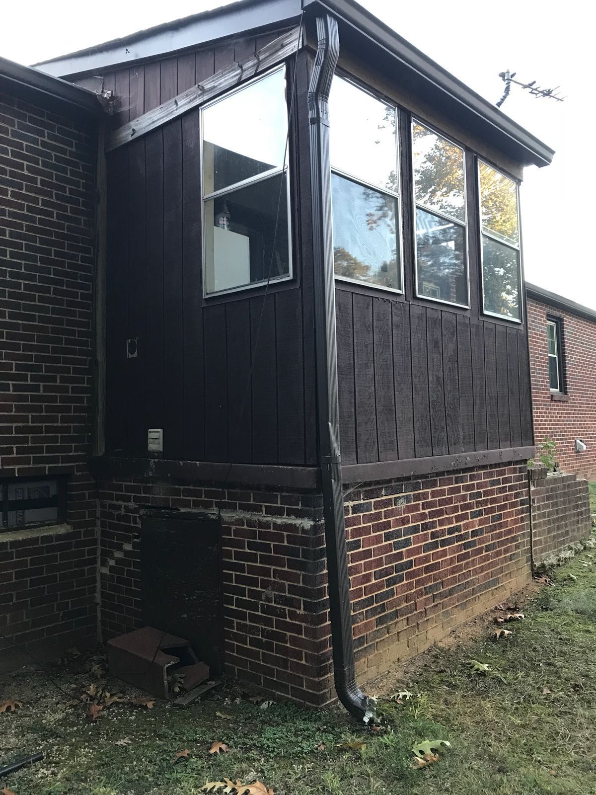 A brick house with a screened in porch and a gutter.