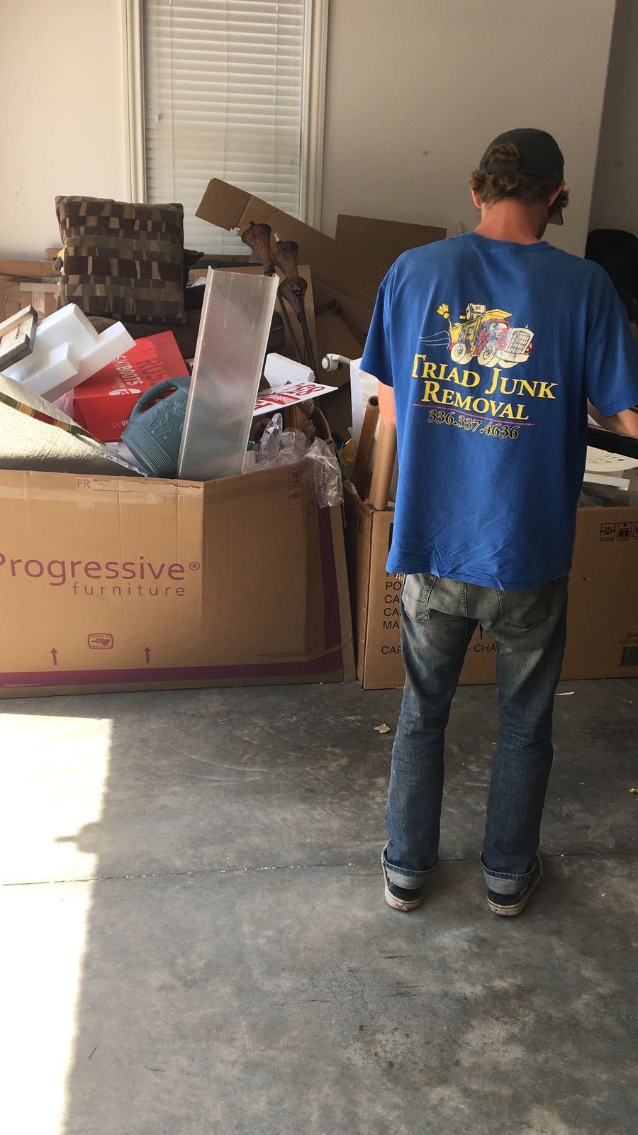 A man in a blue shirt is standing in front of a pile of cardboard boxes.