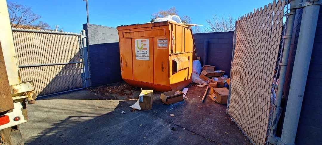 A large orange dumpster is sitting next to a chain link fence.