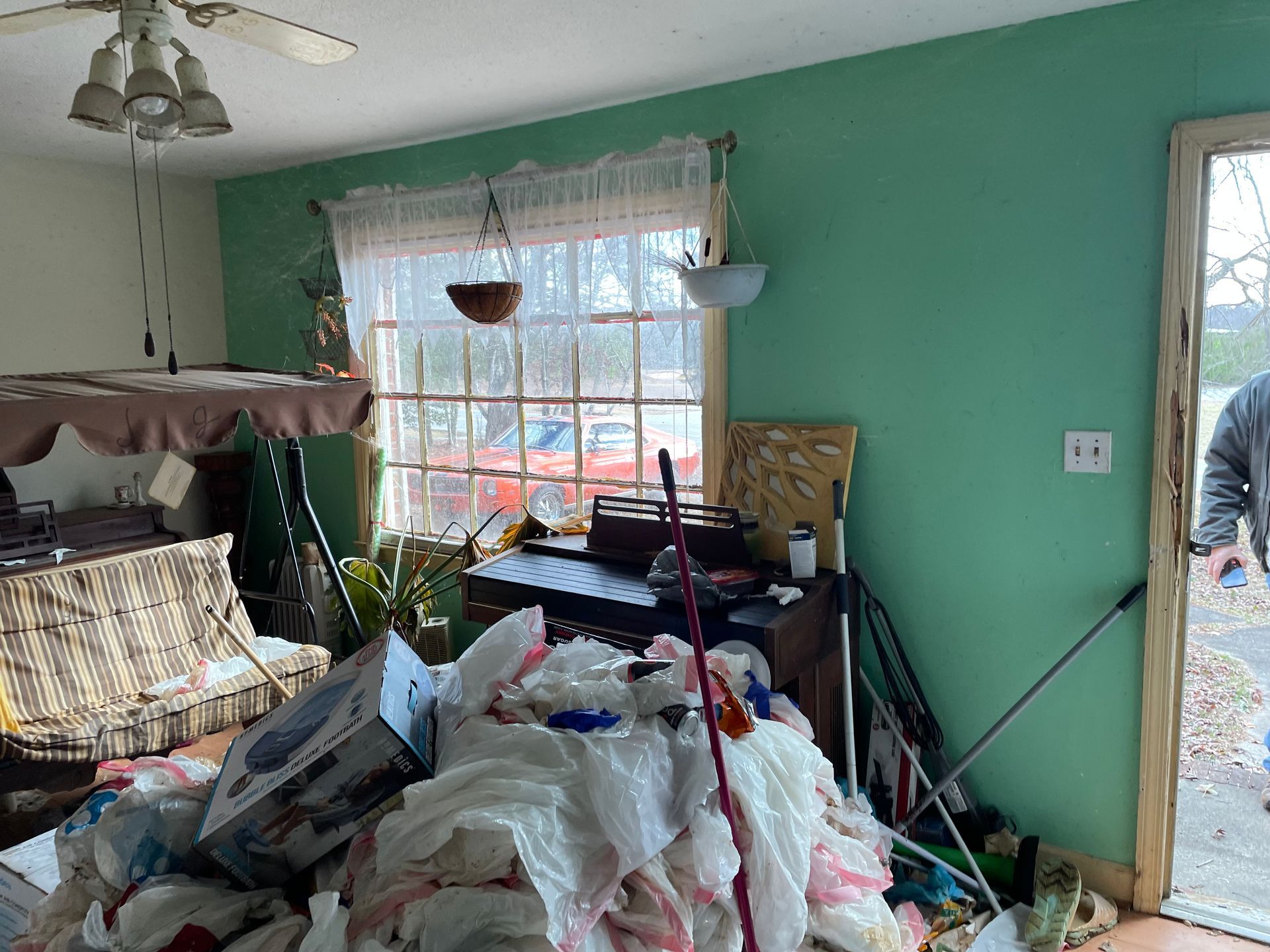 A living room with a lot of trash on the floor and a ceiling fan.