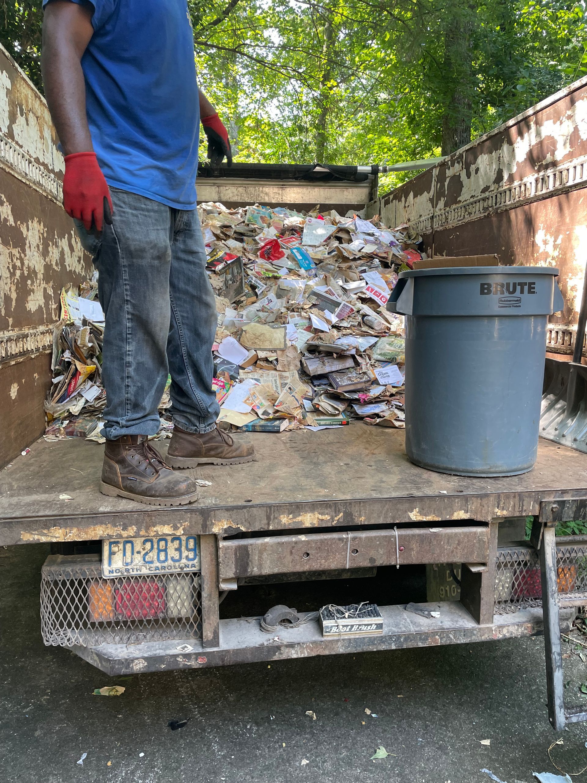 A man is standing on the back of a garbage truck