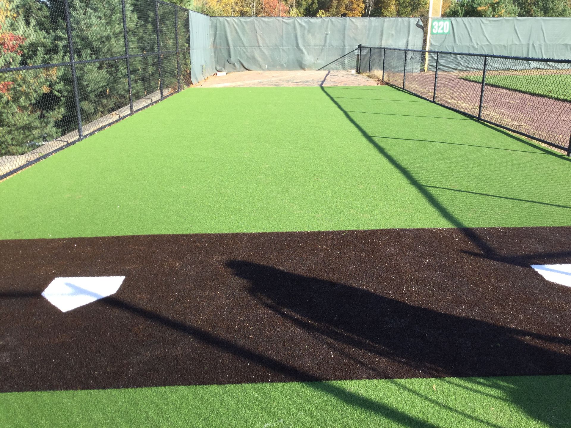 An outdoor baseball or softball batting practice area with green turf, a brown dirt path, and home plate.