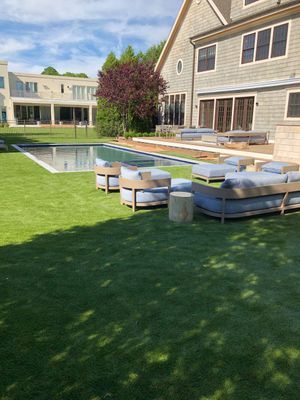A swimming pool surrounded by a green lawn and modern outdoor furniture beside a large house.