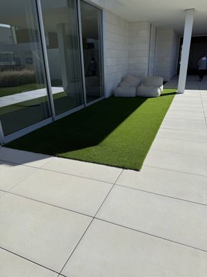 Modern patio featuring light stone tiles, a rectangular patch of artificial green grass, and two floor cushions.