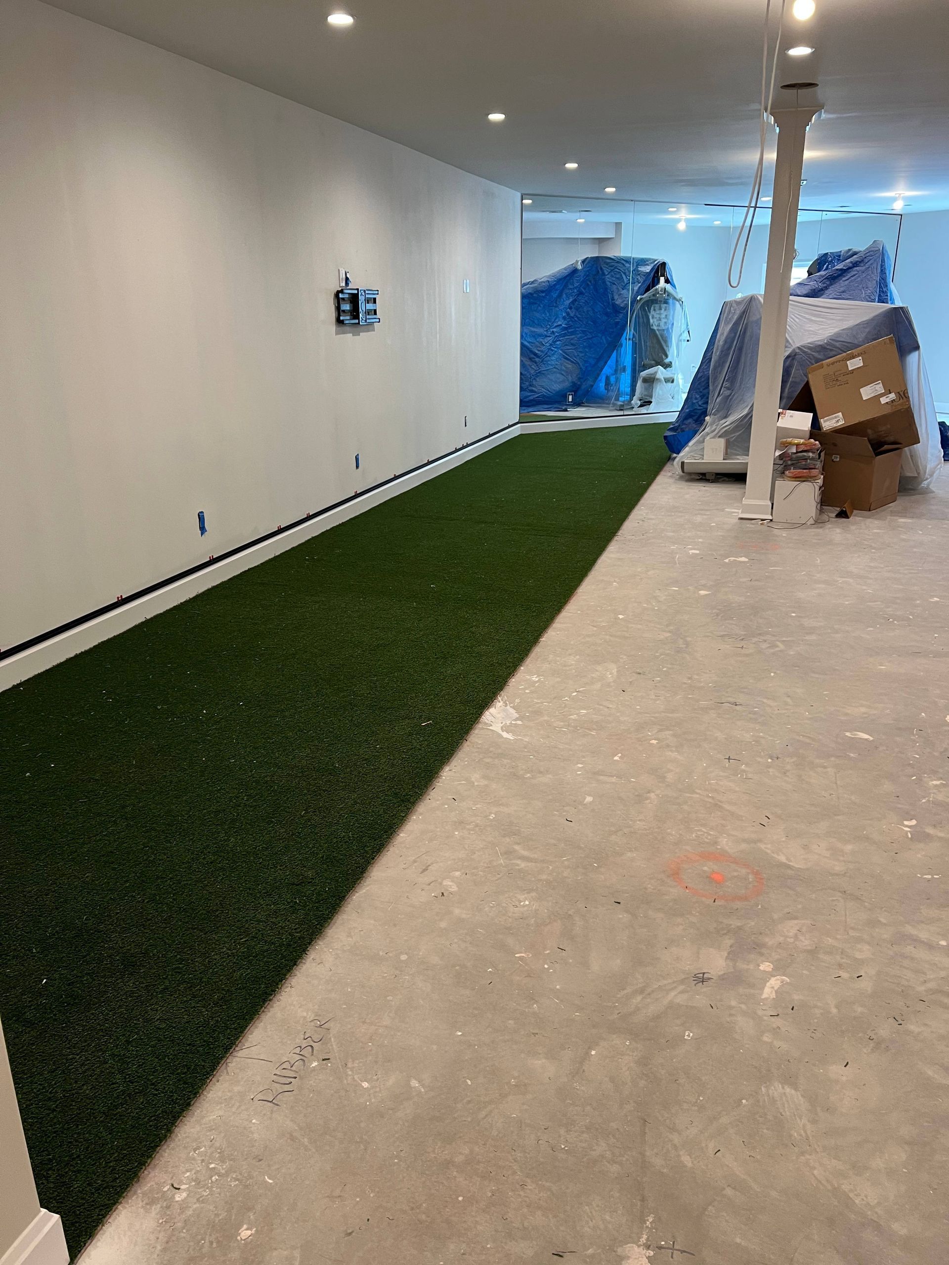 A long strip of artificial grass turf installed on a concrete floor along a white wall in an unfinished basement.