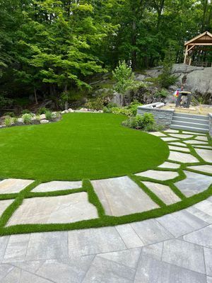 A curved lawn bordered by flagstone pavers and a stone staircase, with a gazebo and trees in the background.