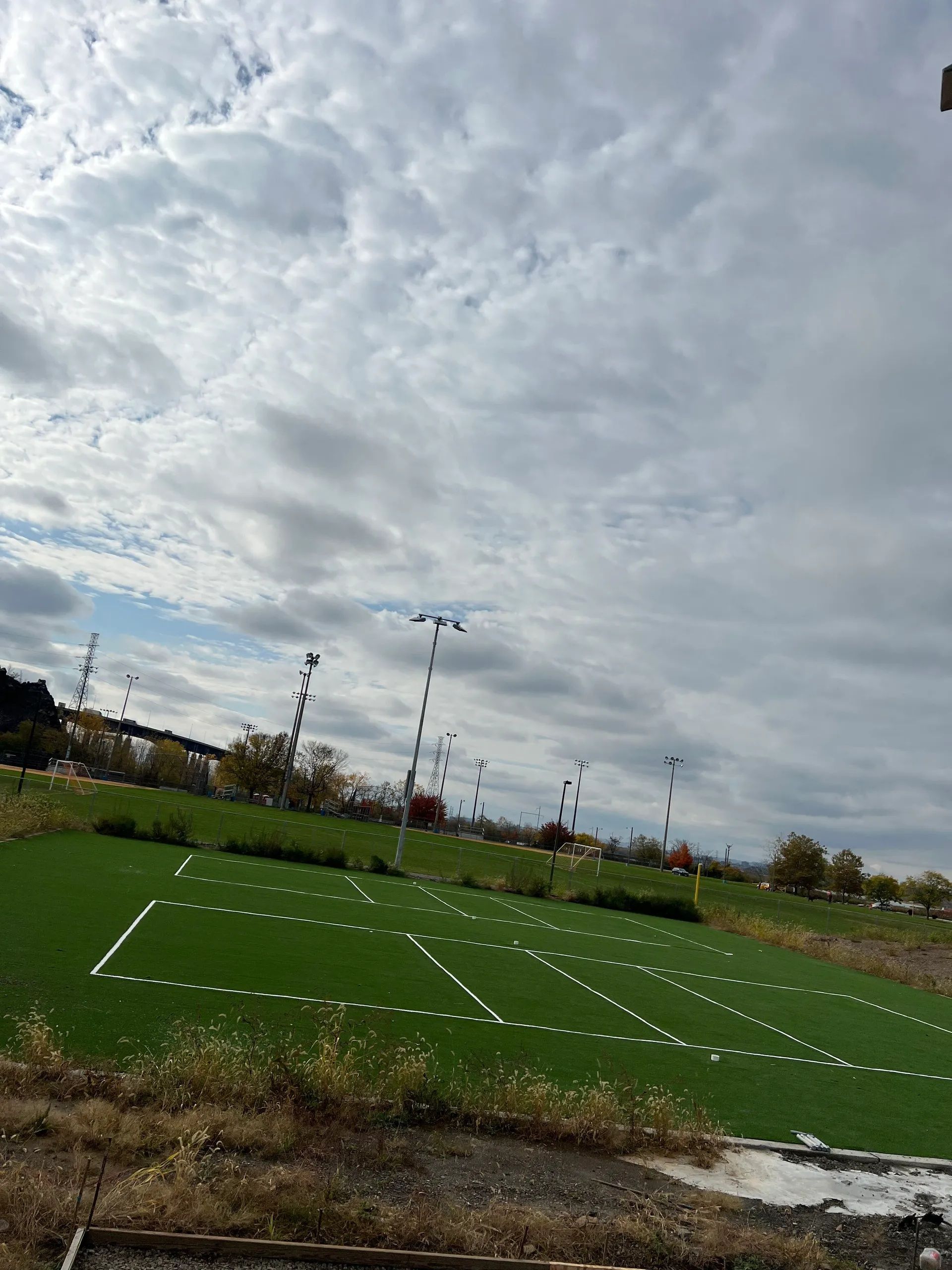 A green sports field with painted white outlines set under a cloudy sky with light poles in the background.