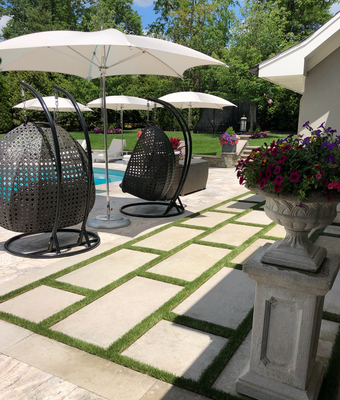 Patio with stone pavers and grass, two dark egg chairs under umbrellas, and a flower-filled stone urn on a pedestal.
