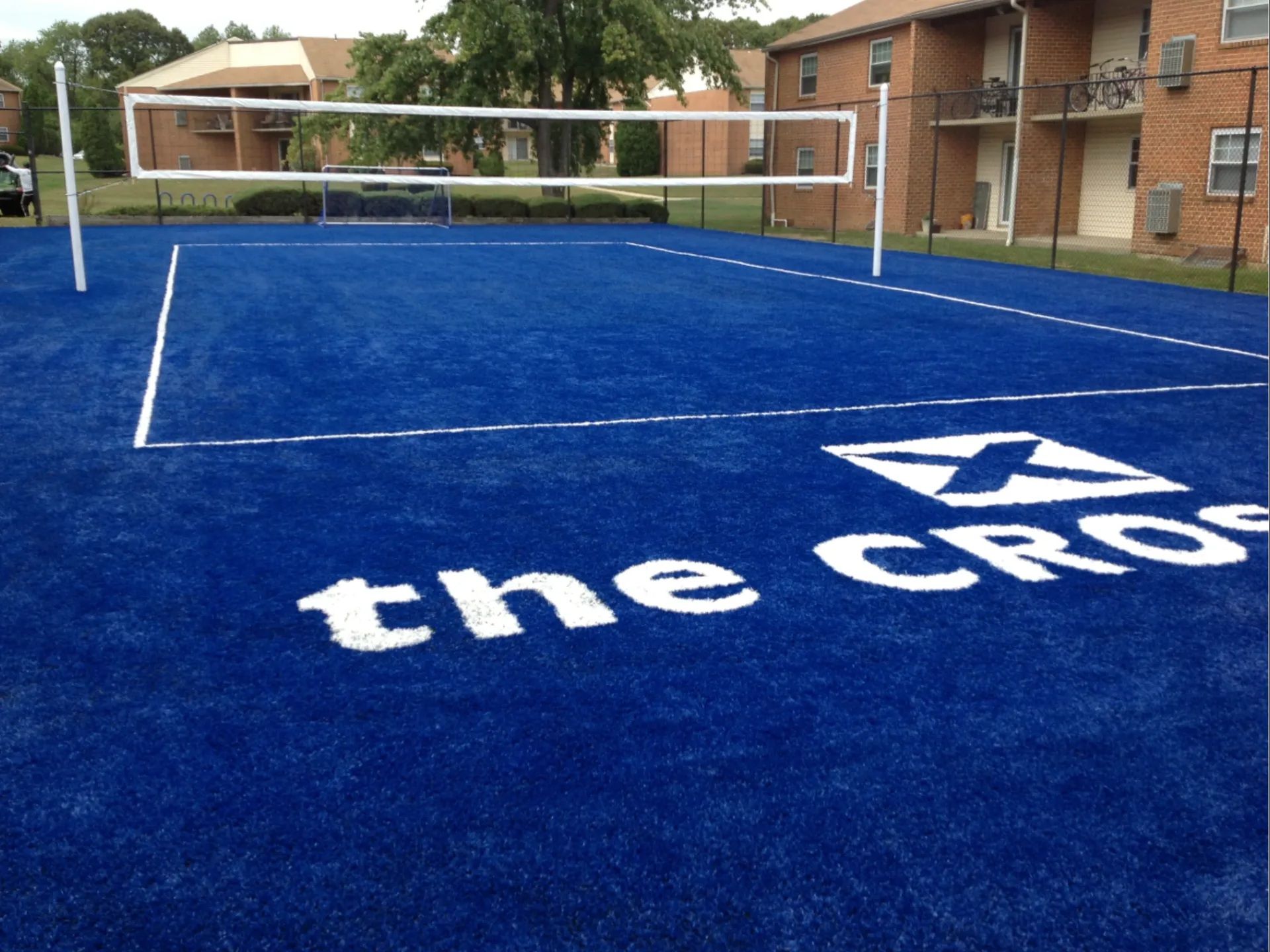A bright blue outdoor court with a volleyball net, featuring the white text 