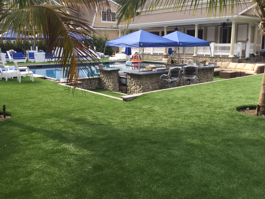 Backyard pool area with a stone swim-up bar, two blue canopy tents, patio furniture, and a manicured green lawn.