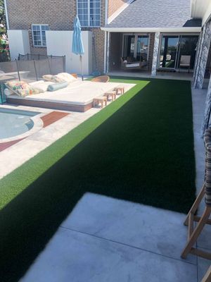 An outdoor patio with a swimming pool, a large cushioned daybed, and a patch of artificial turf next to a house.