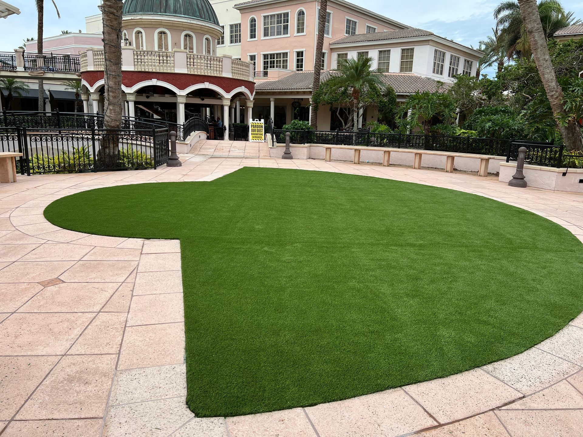 A green, Mickey Mouse-shaped patch of artificial turf set into a light-colored stone patio outside a resort-style building.