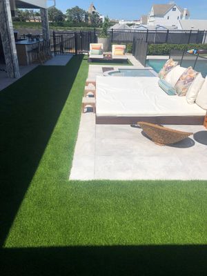 A backyard patio with artificial turf, a large sunbed, loungers, and a swimming pool on a sunny day.
