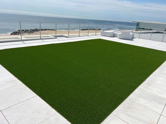 A rectangular patch of green artificial turf on a white-tiled patio overlooking the beach and ocean.