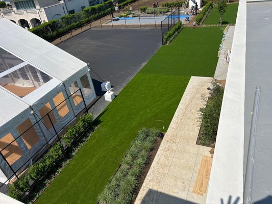 High-angle view of a backyard featuring a large event tent, a paved area, green lawn, stone walkway, and landscaping.