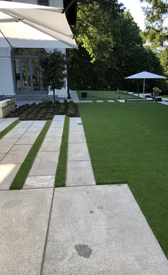 Modern patio with gray stone pavers, grass strips, and a green lawn under two white umbrellas.