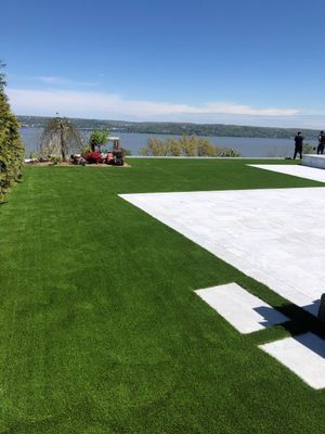 A bright green lawn next to a white stone patio, overlooking a wide river under a clear blue sky.
