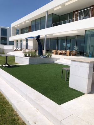 A modern white multi-story house with a lawn, outdoor furniture, and a blue whale tail sculpture.