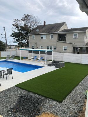 Backyard scene featuring a swimming pool, a patch of artificial turf, a shaded seating area, and a gravel patio.
